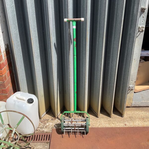 Vintage garden lawn aerator with green handle and spiked rollers.