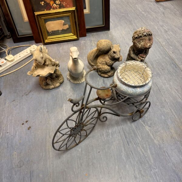 Vintage wire tricycle planter with garden ornaments.