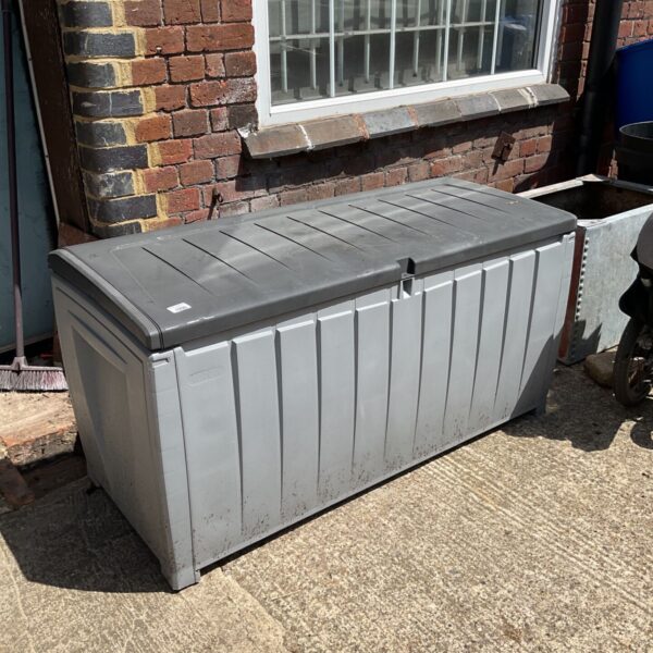 Grey plastic garden storage chest in a backyard setting.