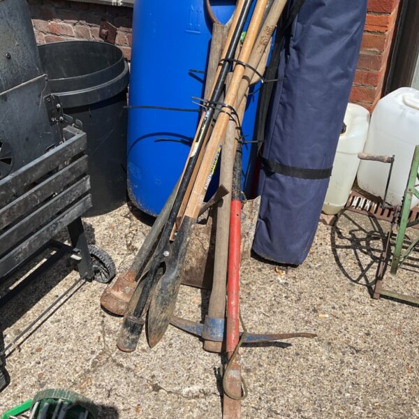 Bundle of used garden tools including a pickaxe and shovels.
