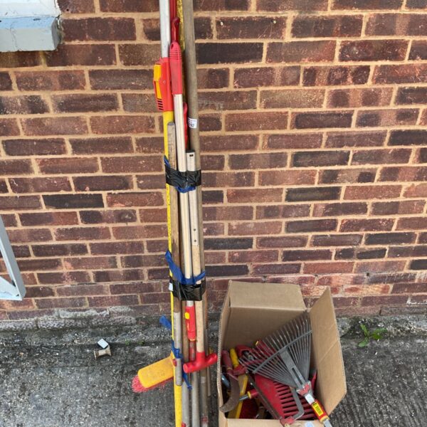 A job lot of used garden tools including a rake and brush.