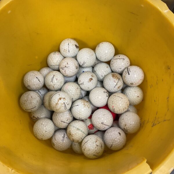 Bucket of used Titleist golf balls for practice and play.