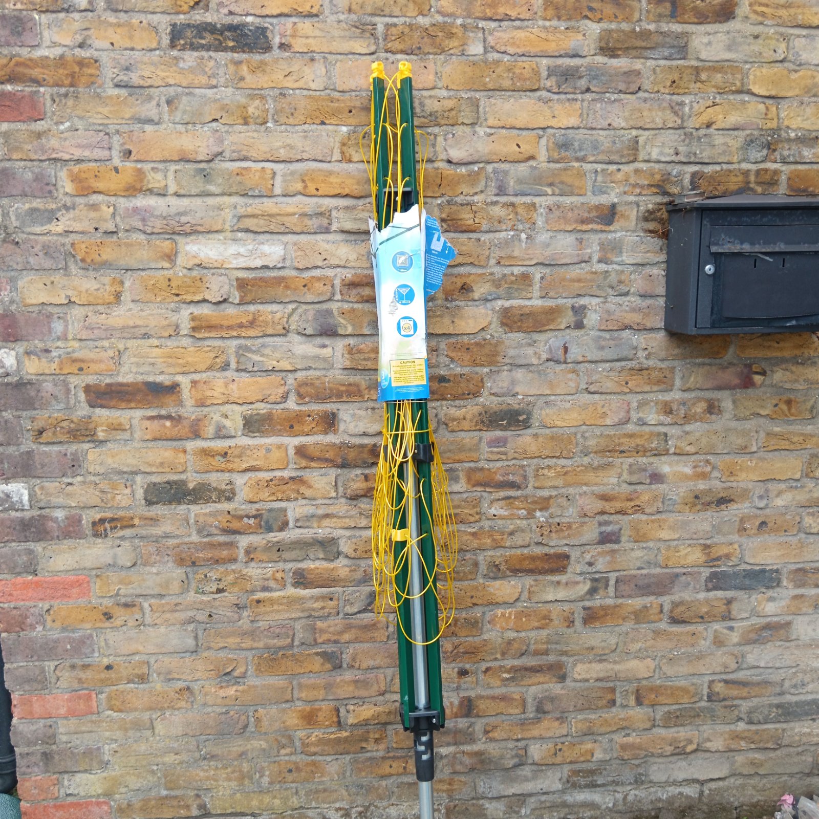 Green and yellow rotary clothes airer in a garden setting.