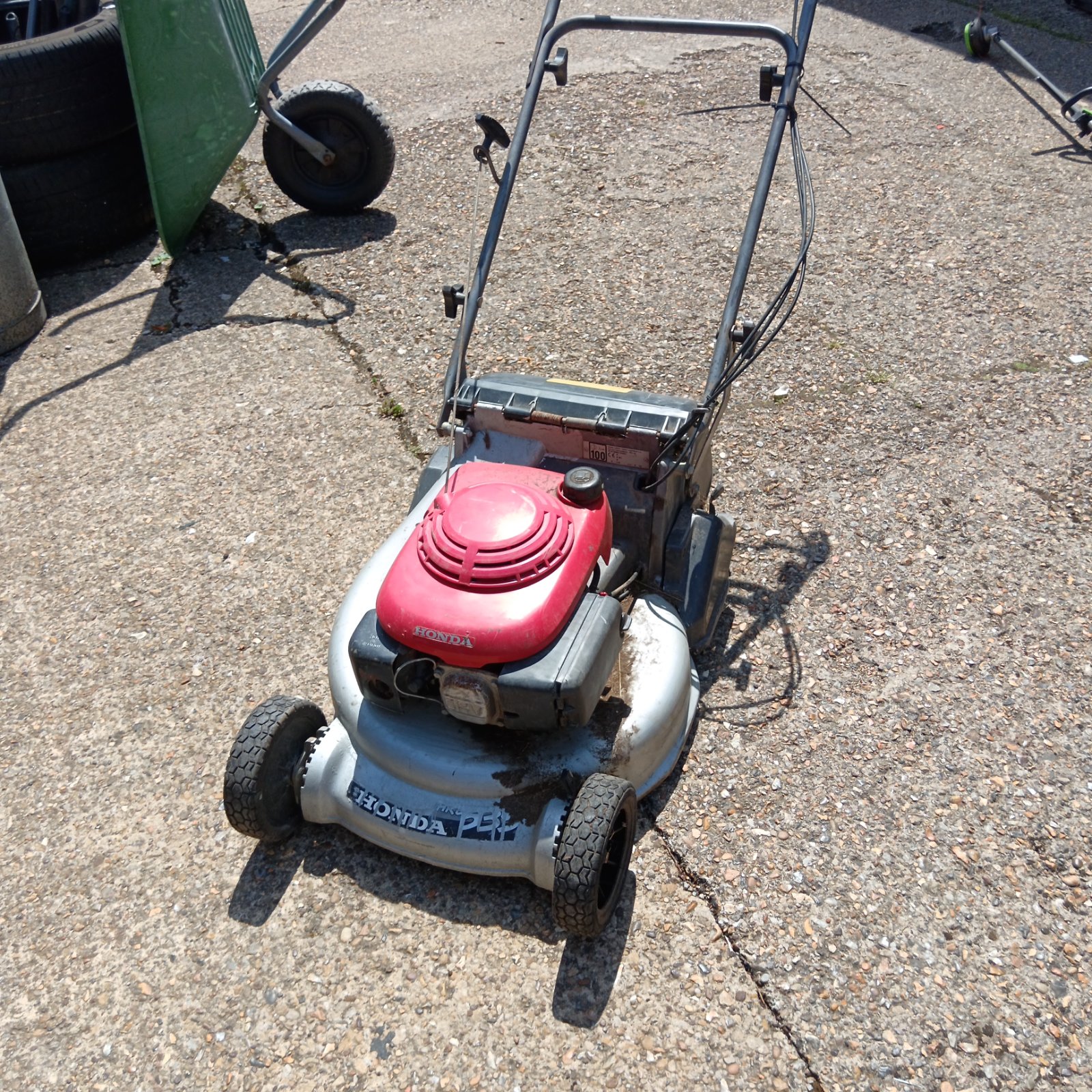 Red Honda 536 petrol lawnmower in a garden setting.