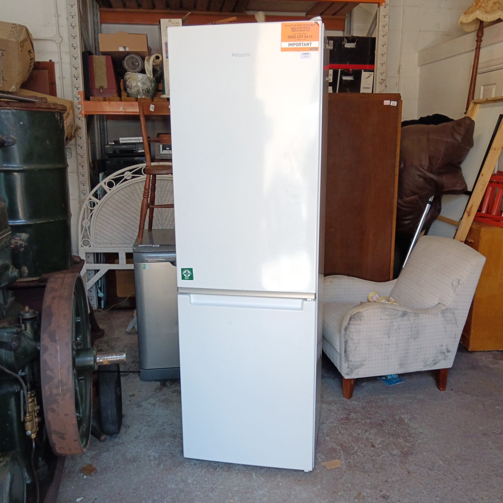 White Hotpoint fridge freezer in a cluttered storage area.