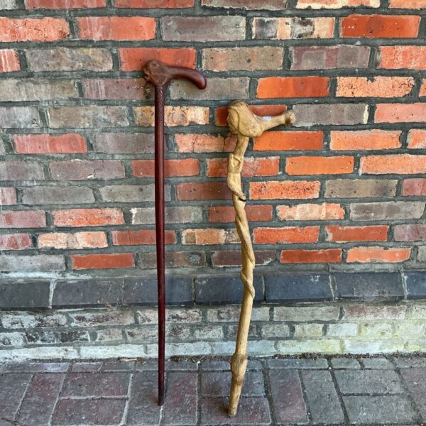 Two vintage wooden walking sticks featuring carved faces on handles