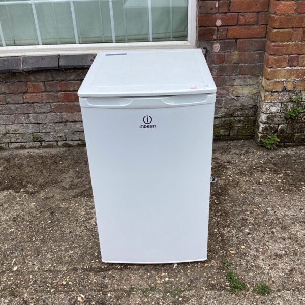 White Indesit chest freezer standing outside on paving.