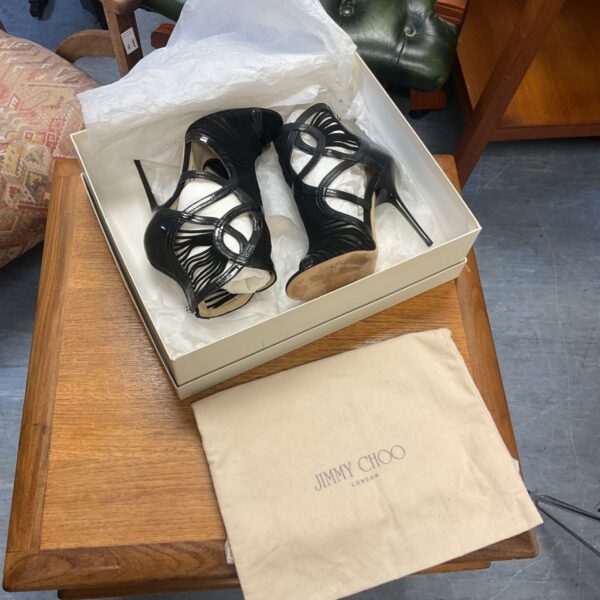 Black Jimmy Choo Samoa patent leather cage sandals on a rug.