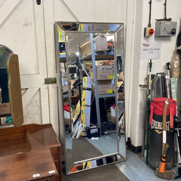 Large bevelled mirror with ornate frame in a cluttered space.