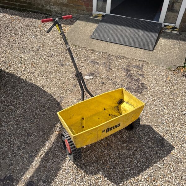Yellow Ortho garden seed spreader with wheels and push handle.