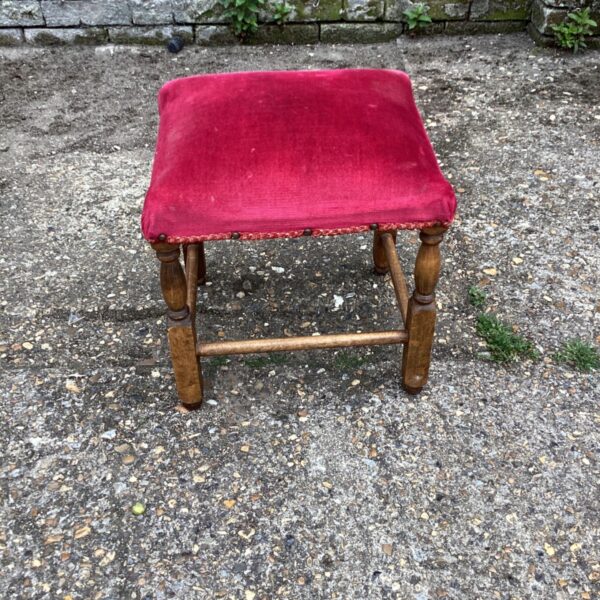 Vintage red upholstered foot stool with wooden legs.