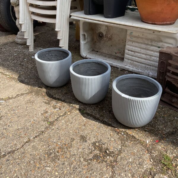 Three ribbed terracotta garden planters displayed outdoors.