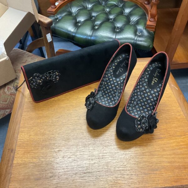 Ruby Shoo black heels with red floral details on a green background.