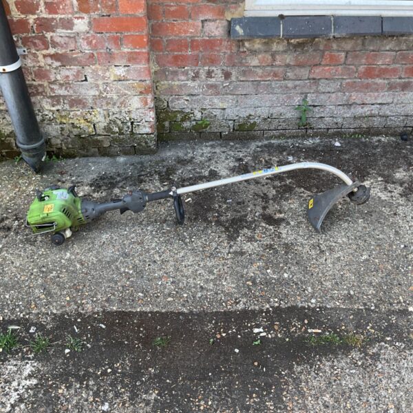 Ryobi petrol grass trimmer against a brick wall.