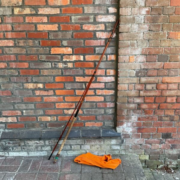 Vintage Shakespeare Alpha fishing rod leaning against brick wall.