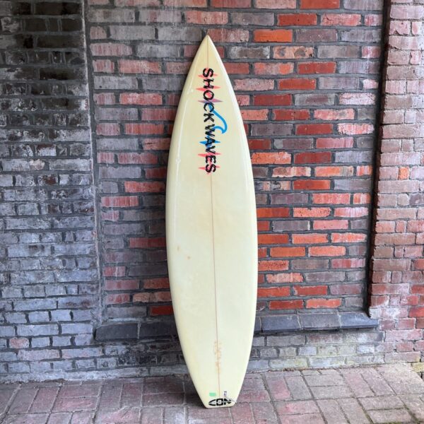 Vintage Shockwaves surfboard leaning against a brick wall.