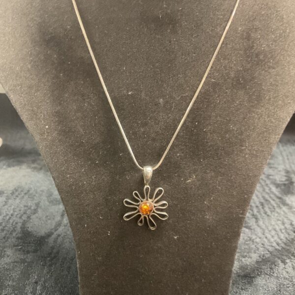 Close-up of silver amber pendant necklace with floral design.