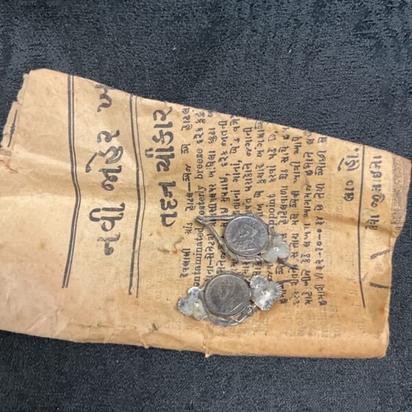 Antique silver coin brooches on aged eastern newspaper fragment.