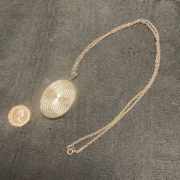 Intricate silver locket necklace with radiating engraving.