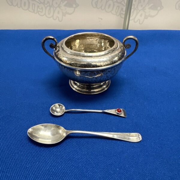 Antique silver sugar bowl with two spoons on blue background.