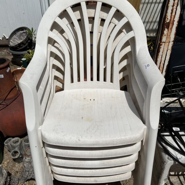 Stack of five white plastic garden chairs for outdoor use.