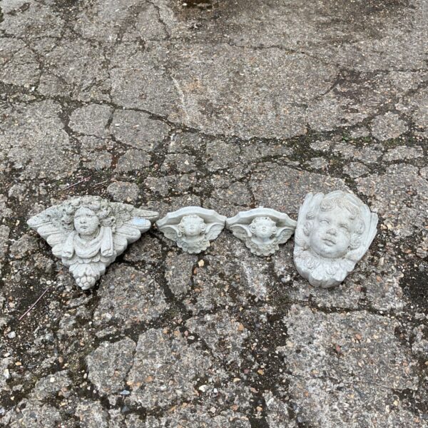 Vintage stone wall ornaments featuring cherub faces in a garden setting.