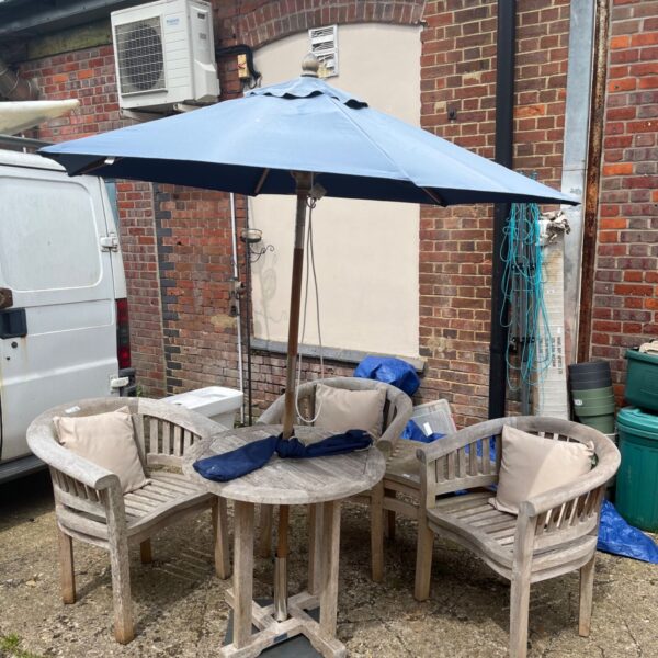 Vintage teak garden furniture set with blue umbrella in a garden.