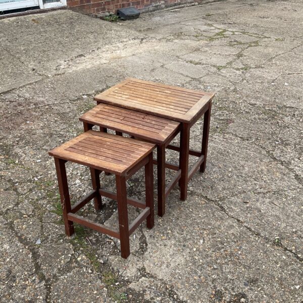 Set of three teak garden tables in a garden setting.