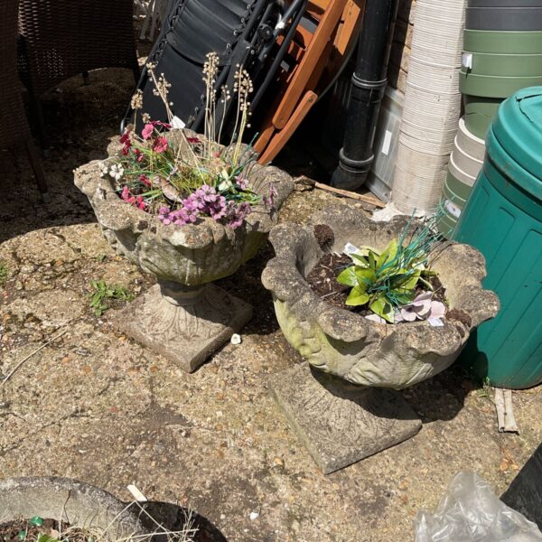 Two terracotta garden planters with colourful floral arrangements in a garden.