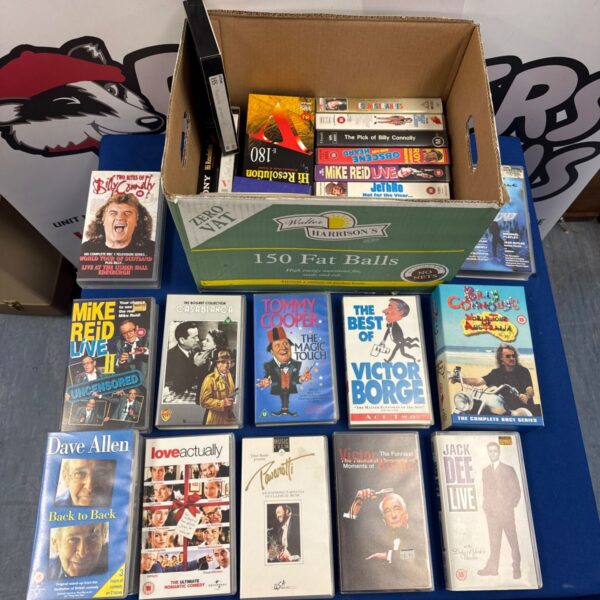 Assorted VHS tapes in a cardboard box, vintage comedy collection.