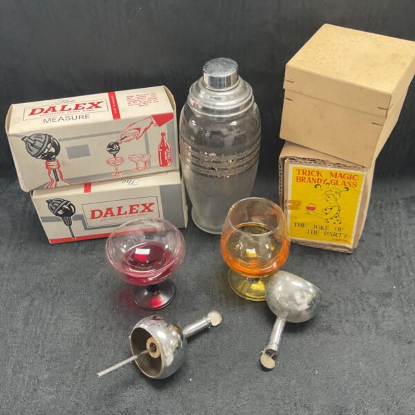Vintage barware lot featuring a Dalex measure and trick drink glasses.
