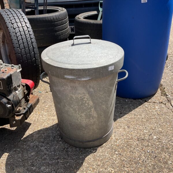Vintage galvanised dustbin with lid in a garden setting.