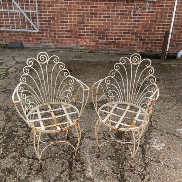 Pair of vintage wrought iron garden chairs in a garden setting.