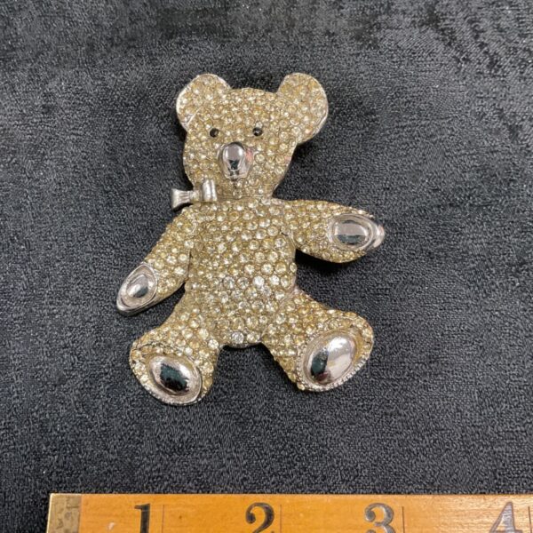 Sparkling vintage jewelled teddy bear brooch on dark fabric.