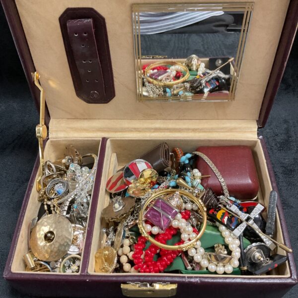 Vintage jewellery box overflowing with costume jewellery and brooches.