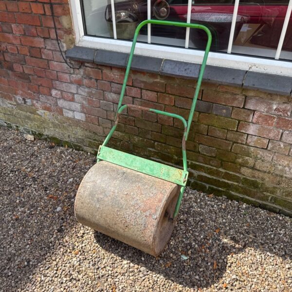 Vintage metal garden roller in a garden setting.