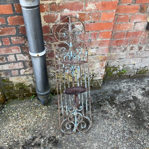 Ornate vintage metal plant holder for wall mounting in a garden setting.