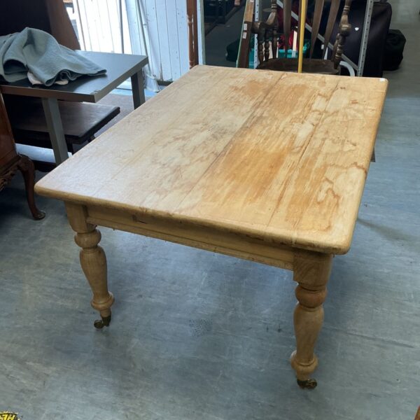 Vintage pine farmhouse table with turned legs and wheels.