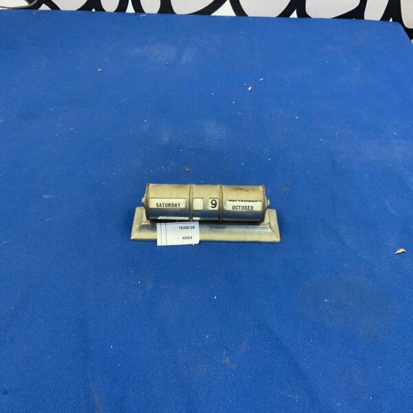 Vintage metal rolling day date calendar on a surface.