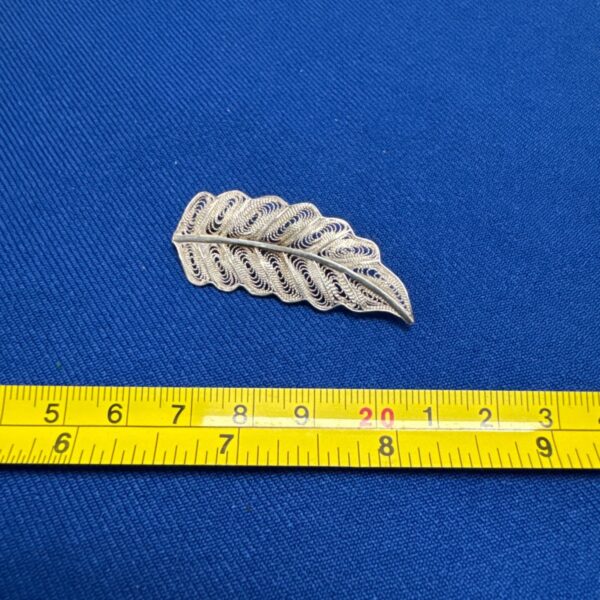 Silver tone leaf brooch measured with a tape measure.