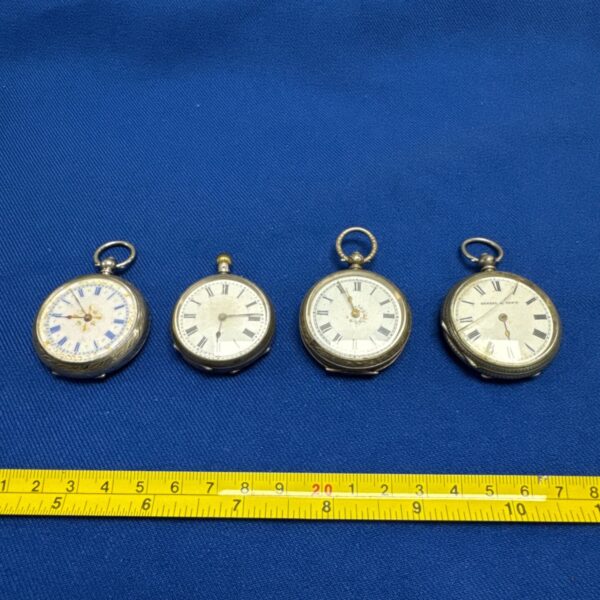 Group of four vintage silver pocket watches on blue background.