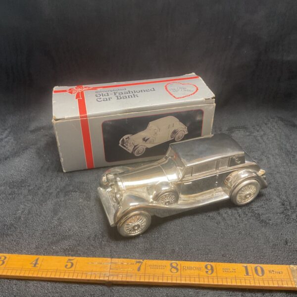 Vintage silverplate classic car money box on a ruler.