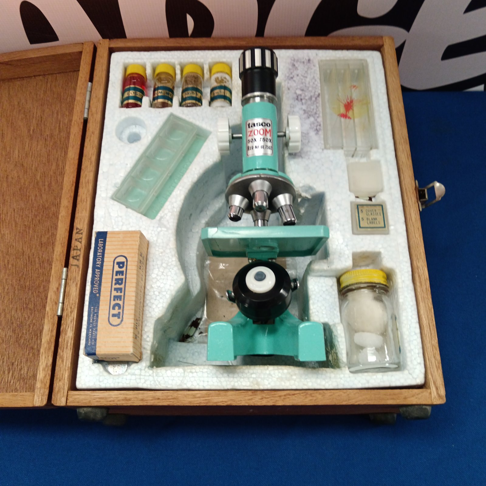 Open case displaying a vintage Tasco microscope and accessories.