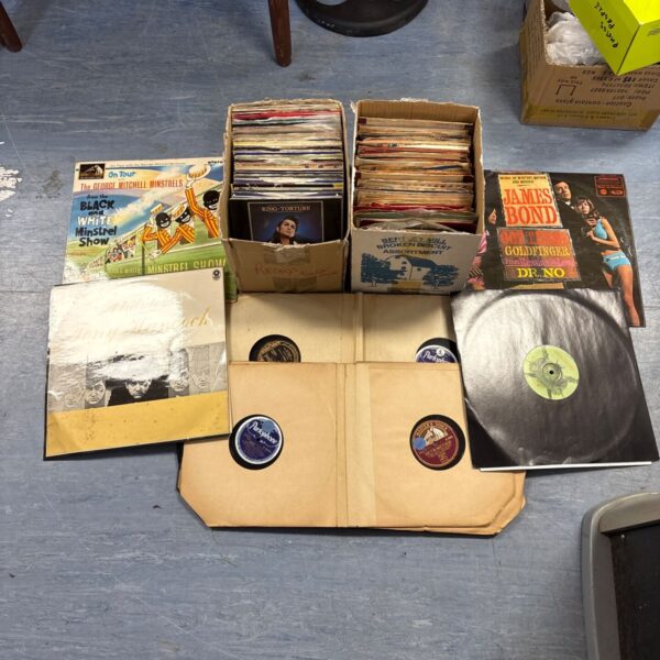 Vintage vinyl record collection in a cardboard box, featuring 7 inch singles.