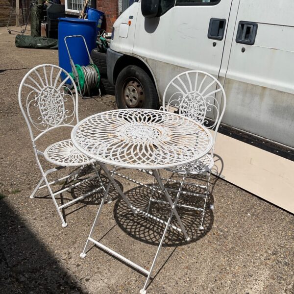 White metal patio set with table and two chairs in a garden.