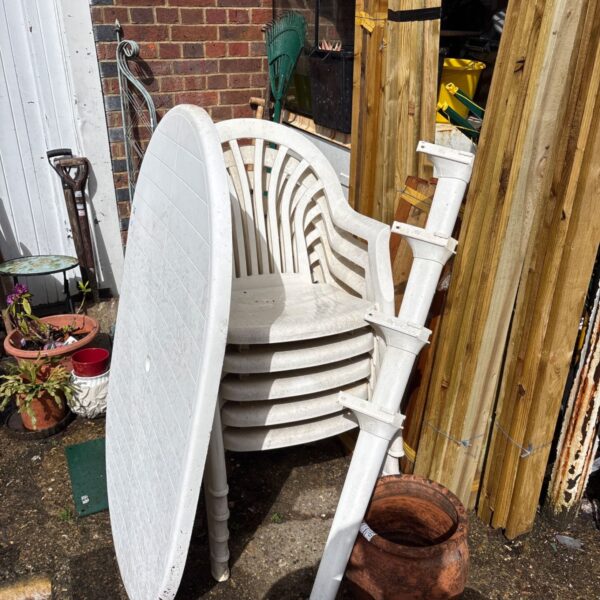 White plastic garden table and five chairs in a garden setting.