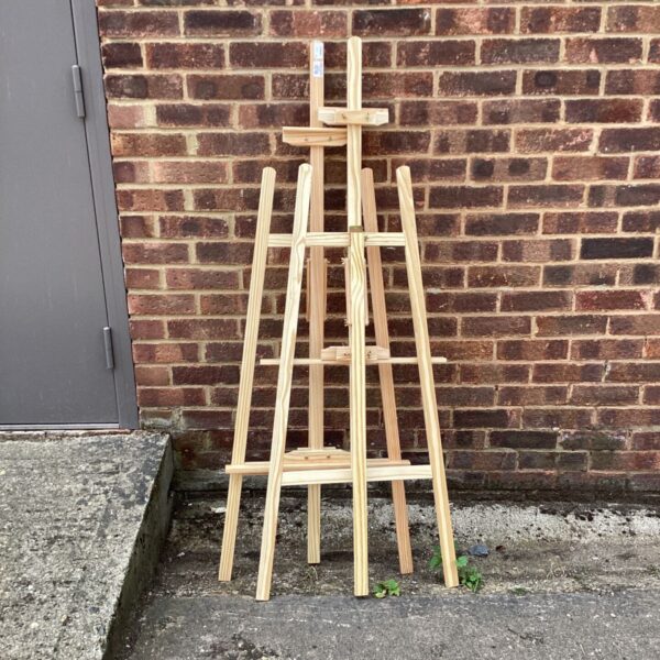 Two wooden artist easels standing against a brick wall.
