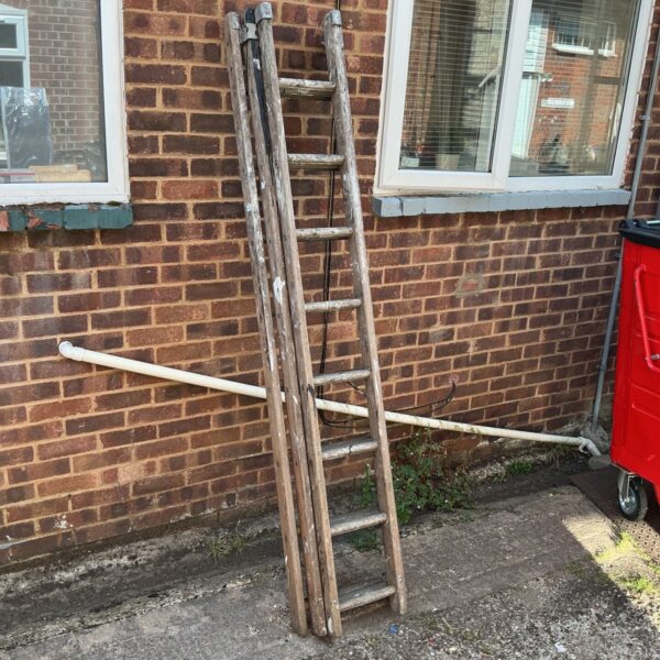 Vintage wooden ladder leaning against a brick wall in a garden.