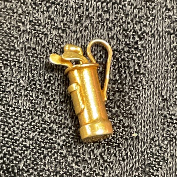 Close-up of vintage 9ct gold golf bag charm on textured background.