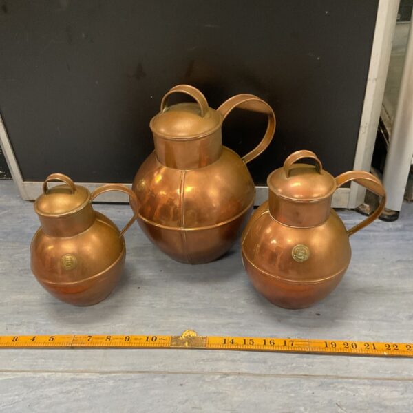 Three antique copper Guernsey creamers in varying sizes.